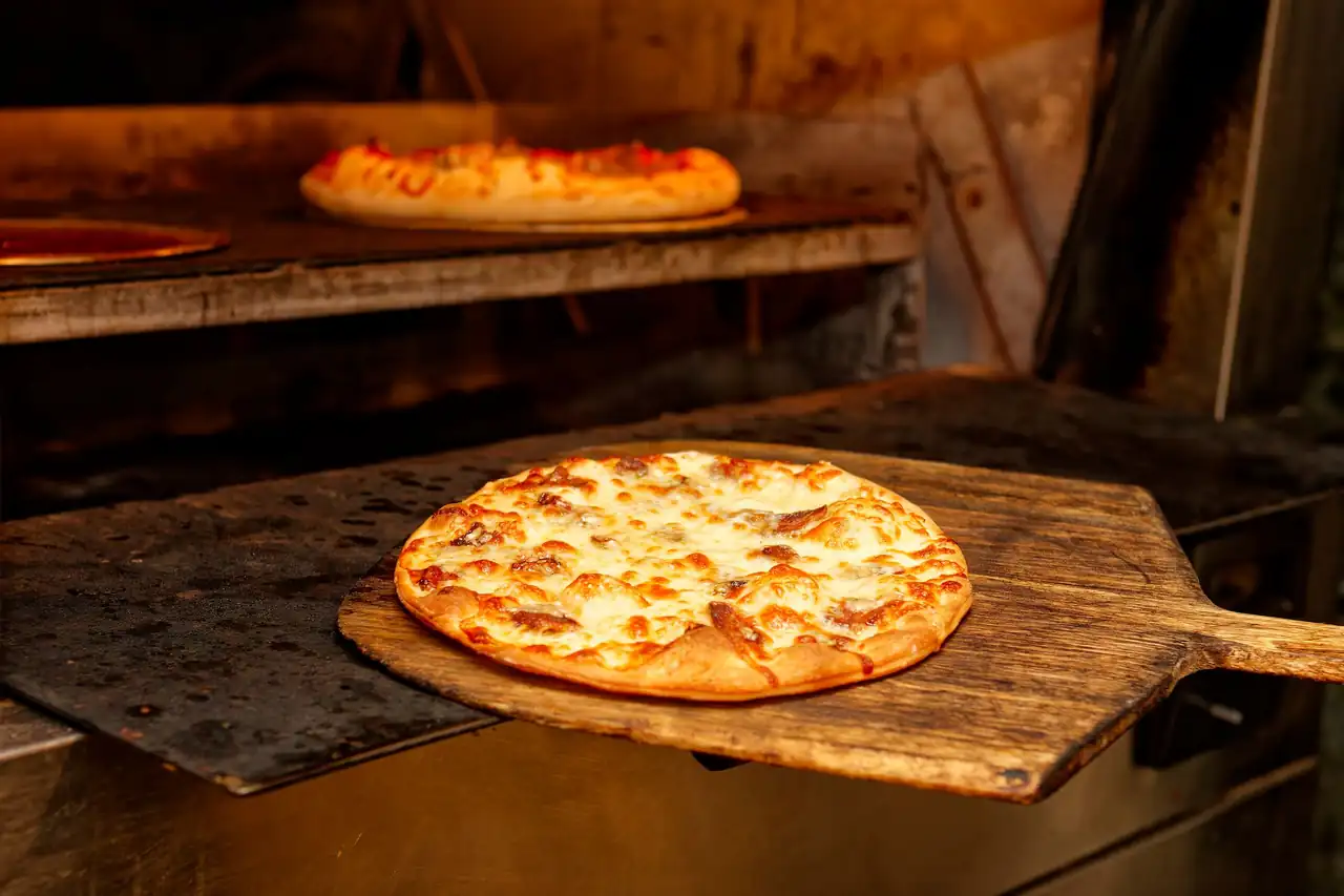 Fire-blistered pizza crust baking inside a stone hearth at Koraven Thessique