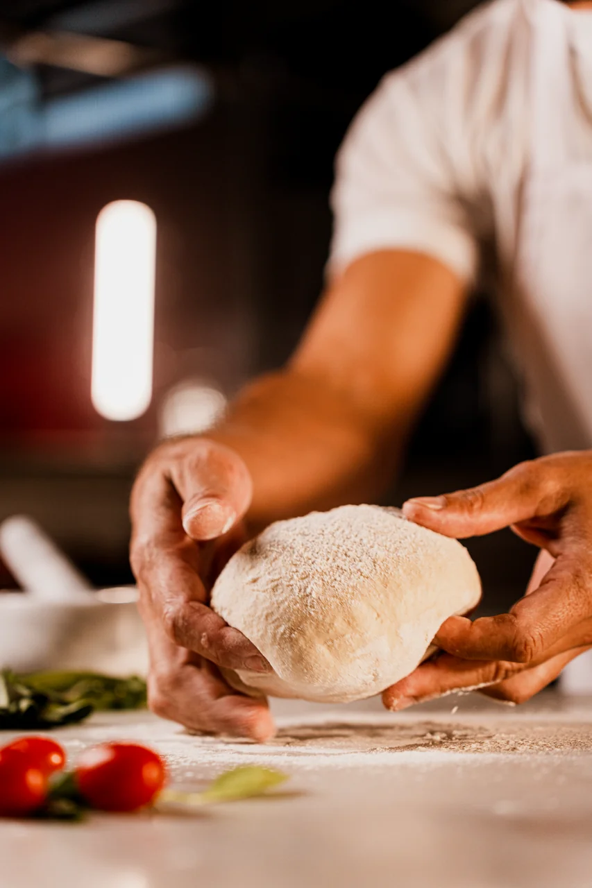 Artisan pizza chef shaping dough on a marble counter dusted with coarse flour