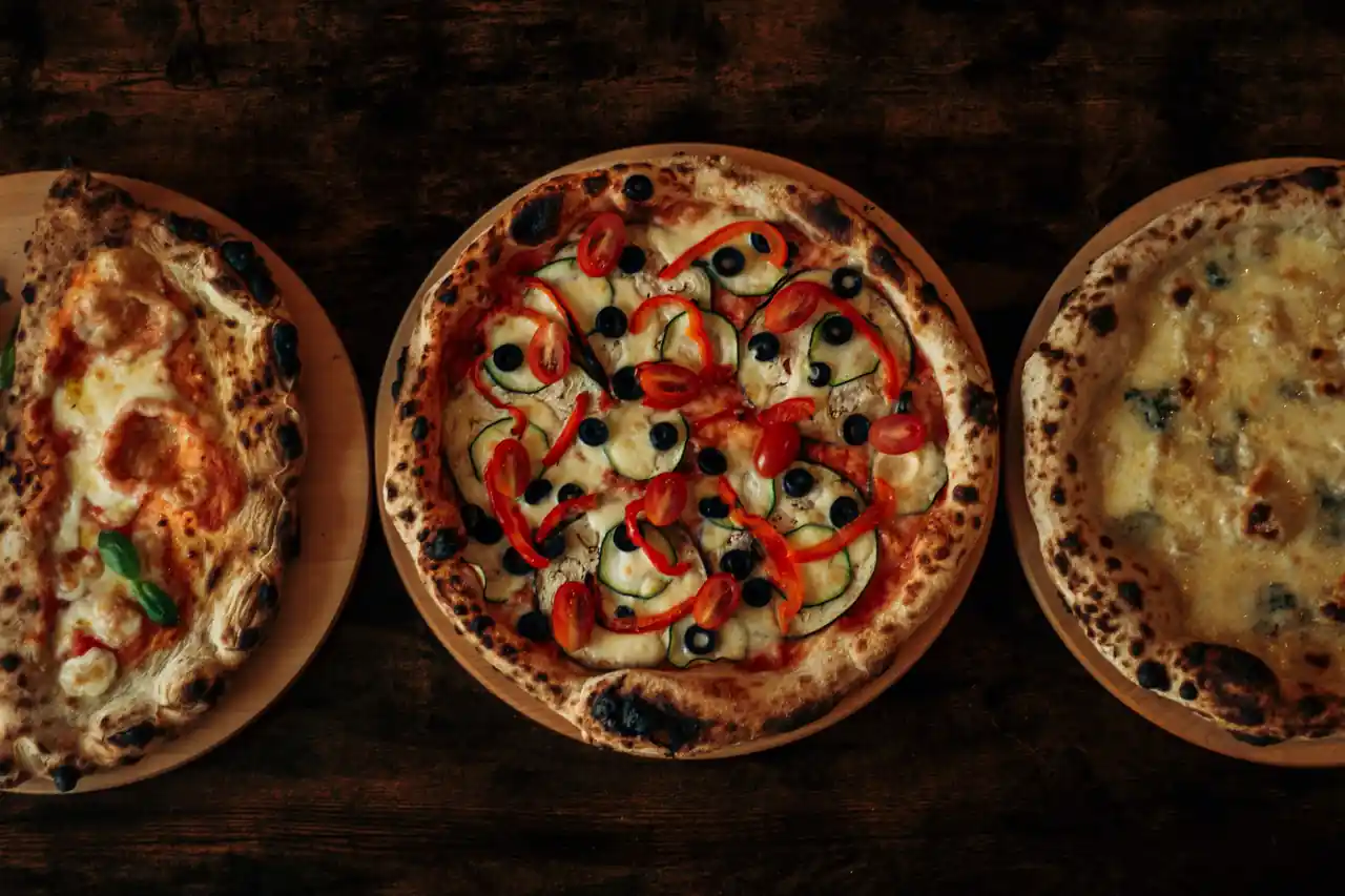 Three artisan wood-fired pizzas with blistered crusts on a wooden dining table