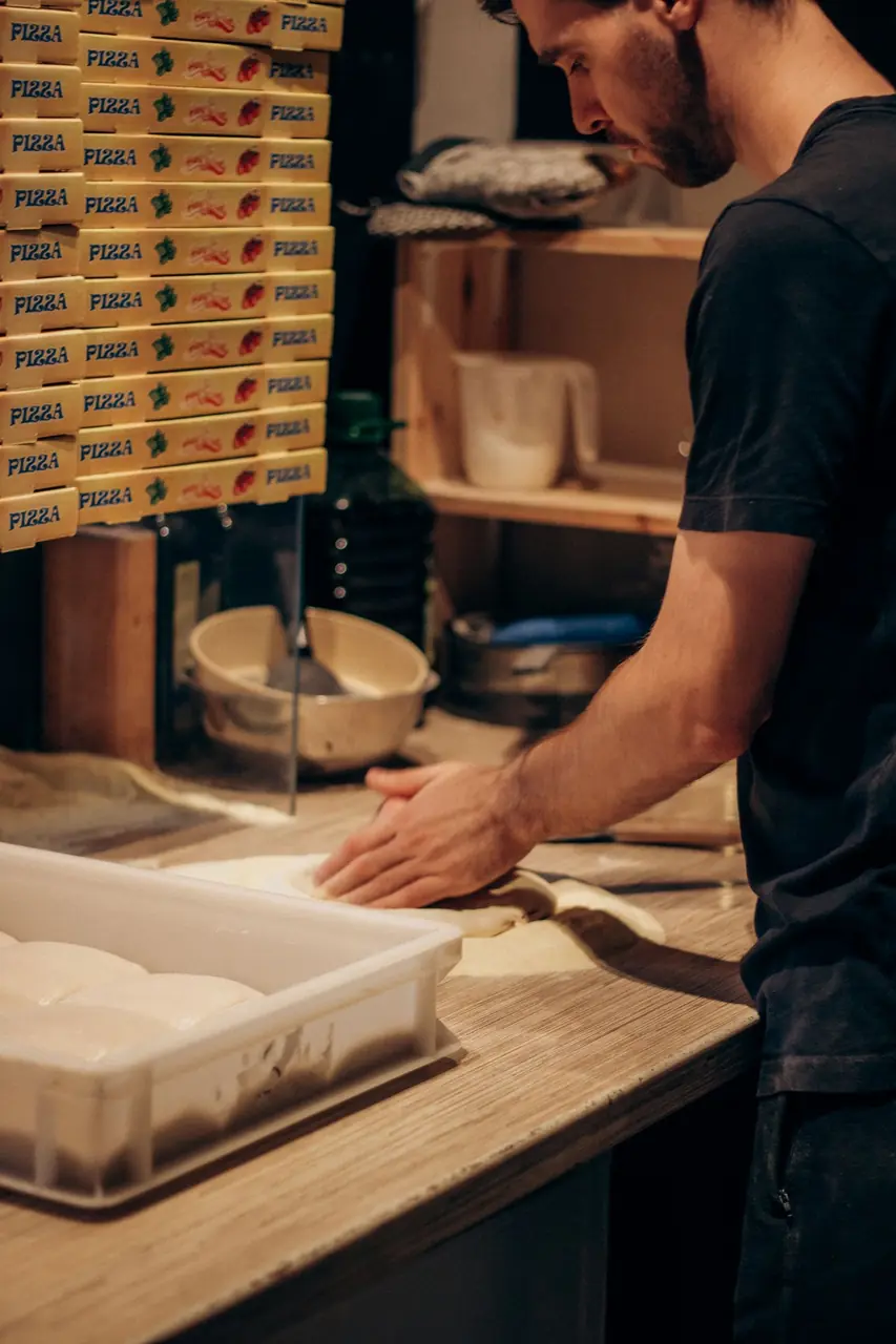 Artisan pizzaiolo dusting flour and shaping dough in the kitchen