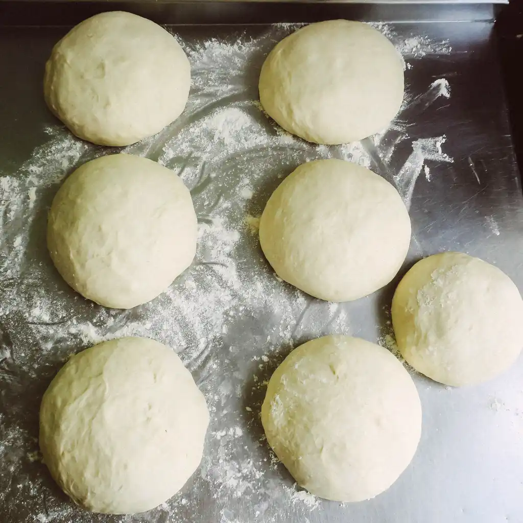 Fresh artisan pizza dough balls prepared on floured prep surface