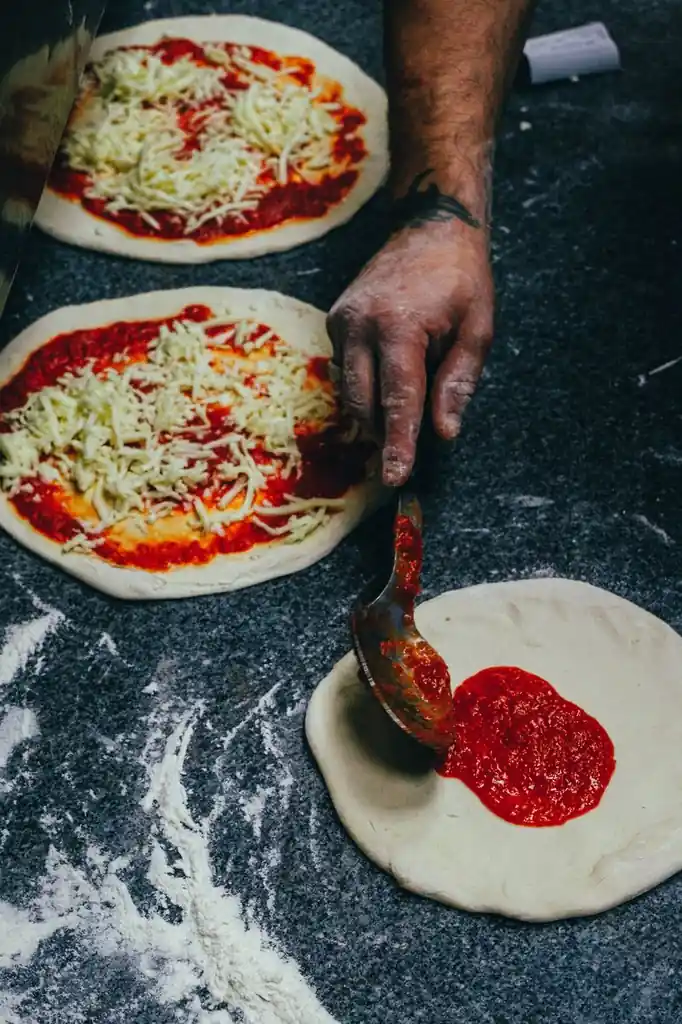 Rich crushed tomato sauce being spread evenly onto pizza dough